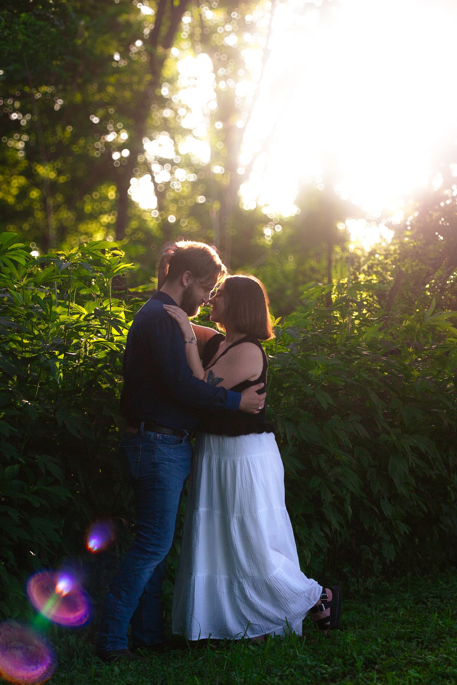 Romantic couple embracing and nearly kissing in lush green forest with golden sunlight.