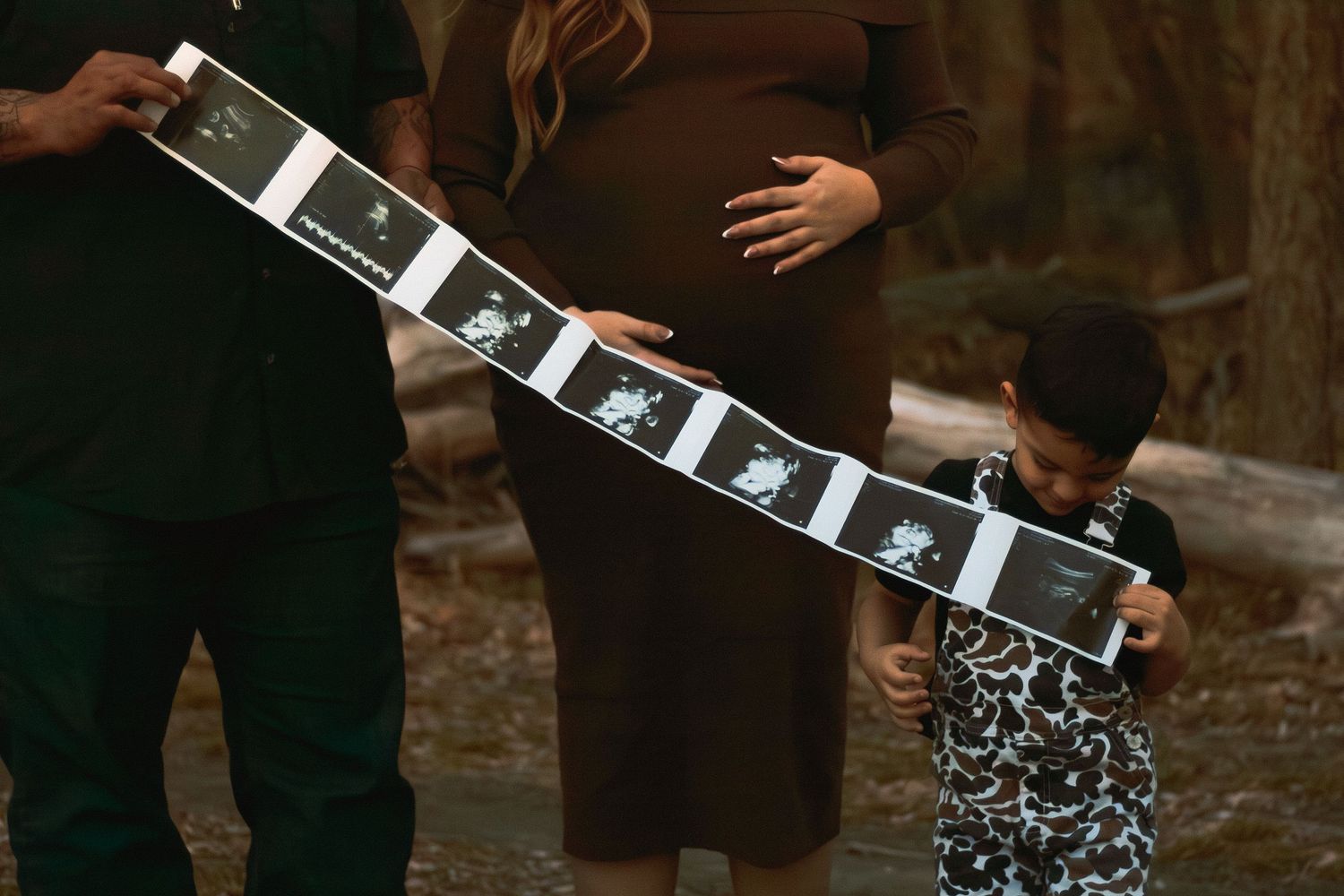 Pregnant woman and child holding ultrasound strip photos outdoors in a maternity announcement photo.