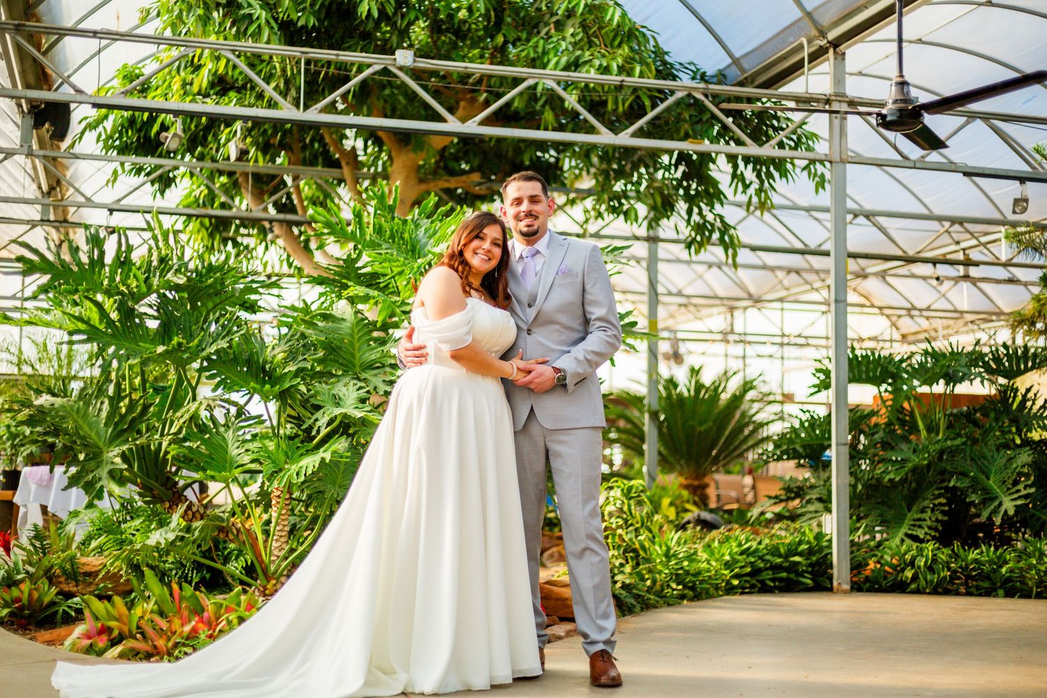 Bride and groom posing together in a lush greenhouse wedding venue surrounded by tropical plants.