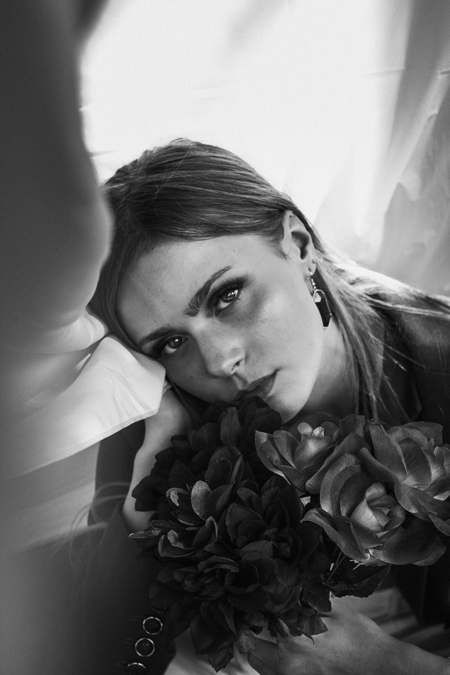 Black and white portrait of woman with flowers leaning against a surface.