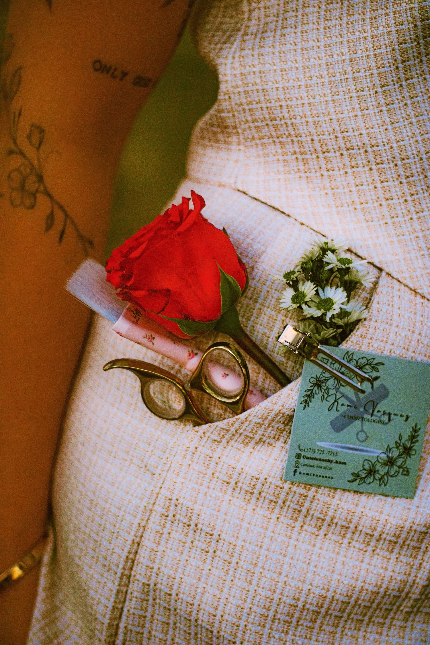 A tweed jacket pocket holds a red rose, vintage scissors, small flowers, and a business card.