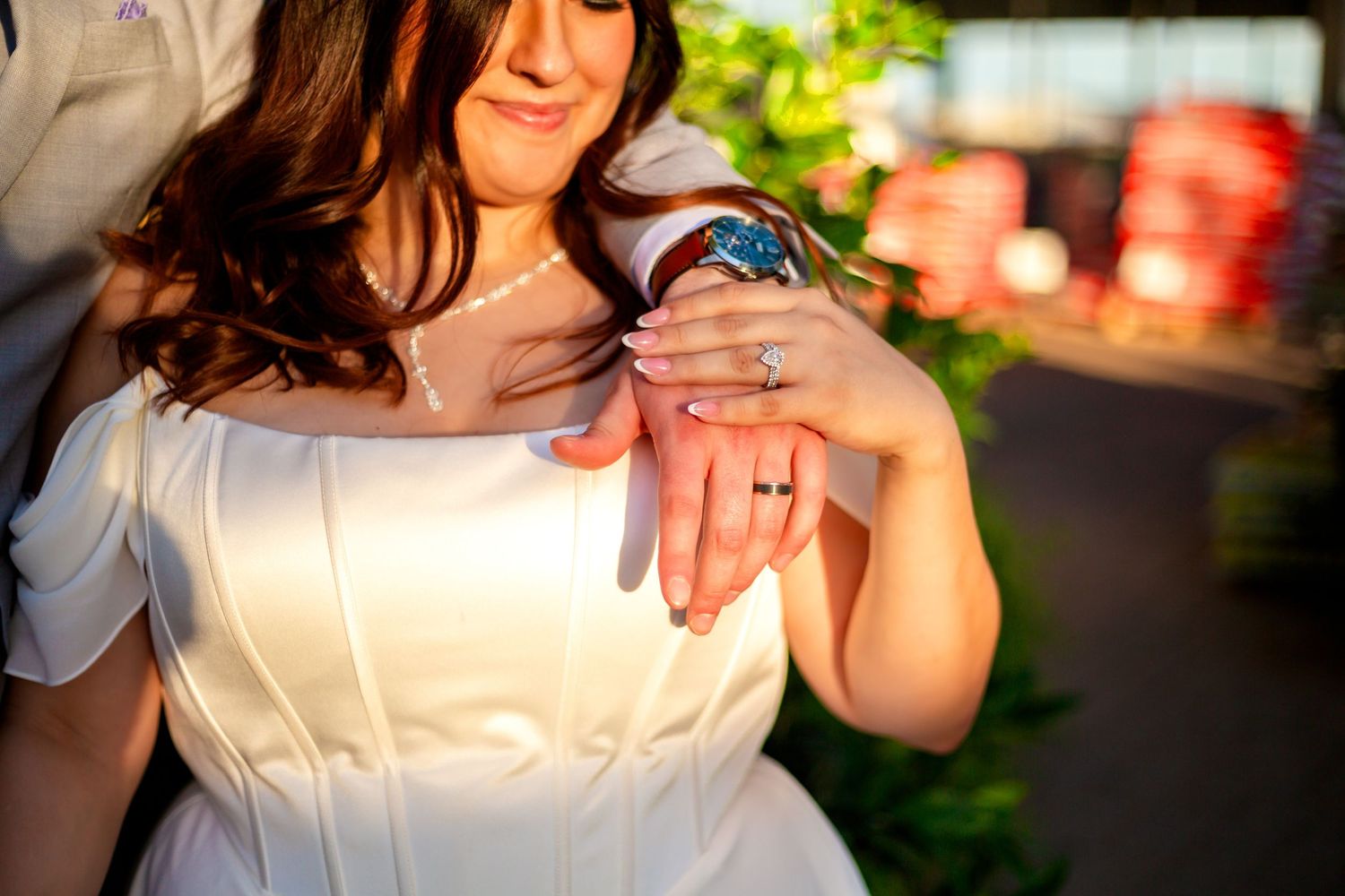 Close-up of bride and groom showcasing wedding rings and watch in warm golden sunset light outdoors.
