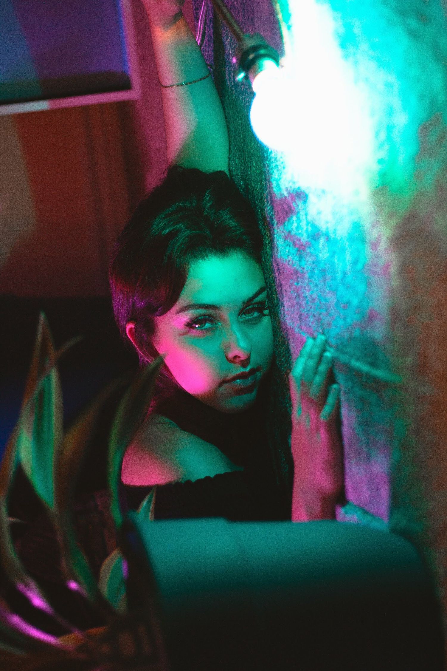 Woman posing dramatically under neon pink and teal lights in dark setting.