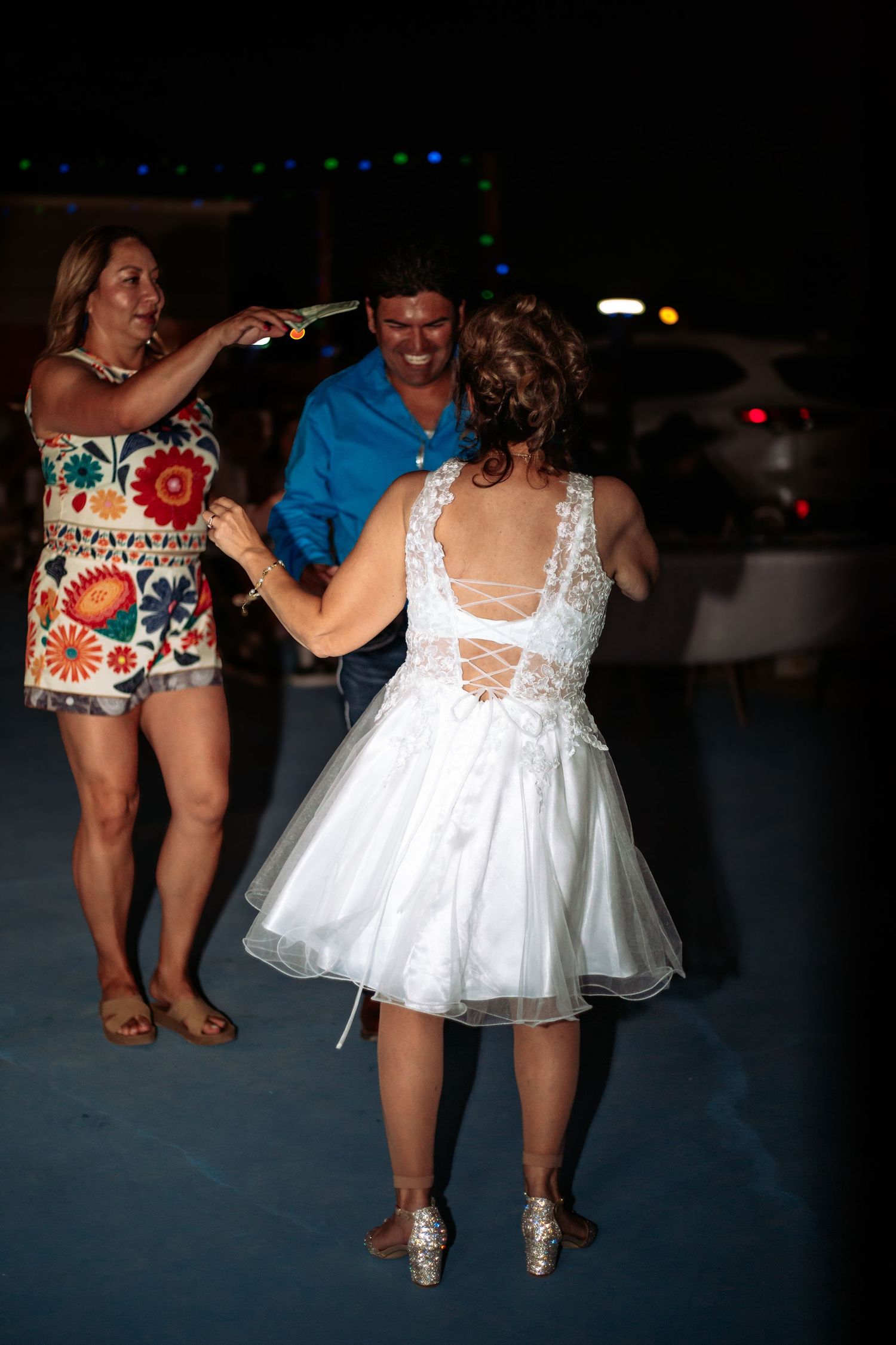 Bride in white dress dancing with guests at outdoor wedding reception at night.