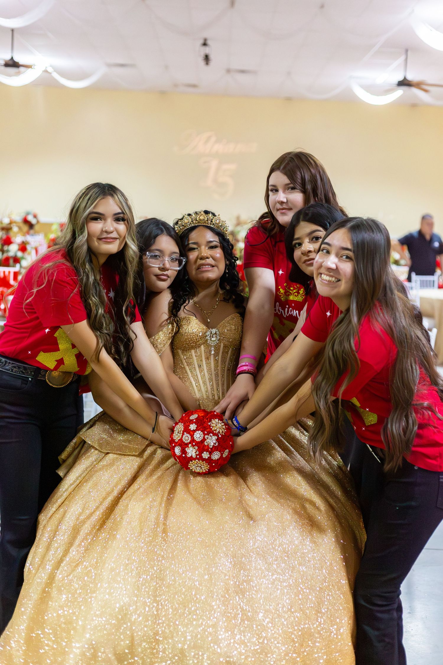 Quinceañera girl in gold gown poses with five friends in red shirts holding bouquet at sweet 15.