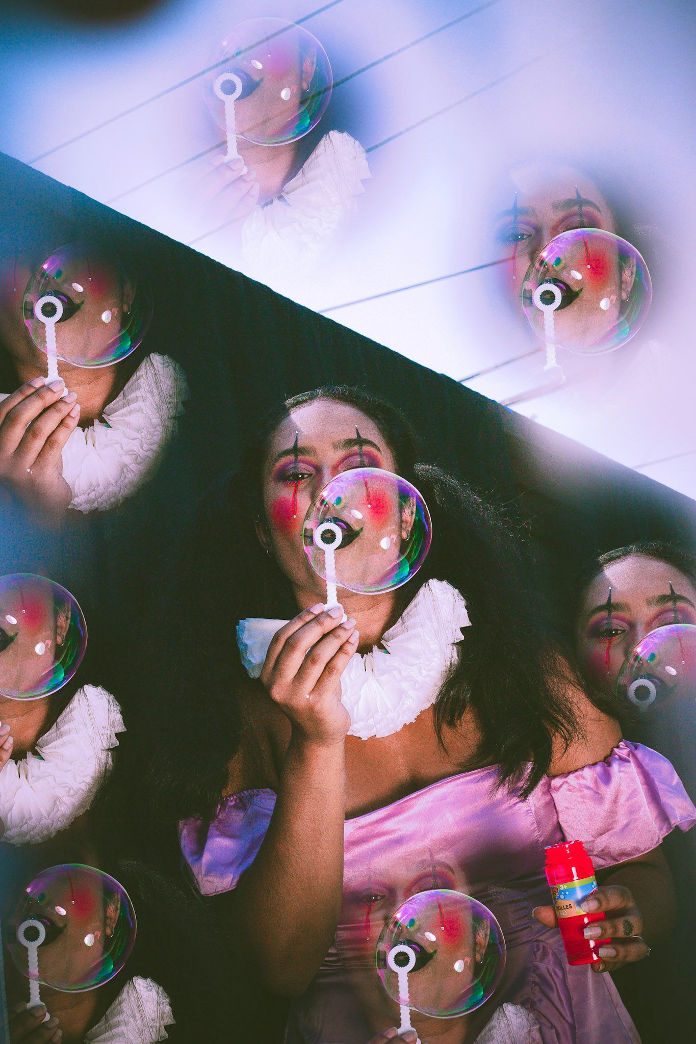 Woman in clown costume blowing soap bubbles reflected in mirrors creating a surreal effect.