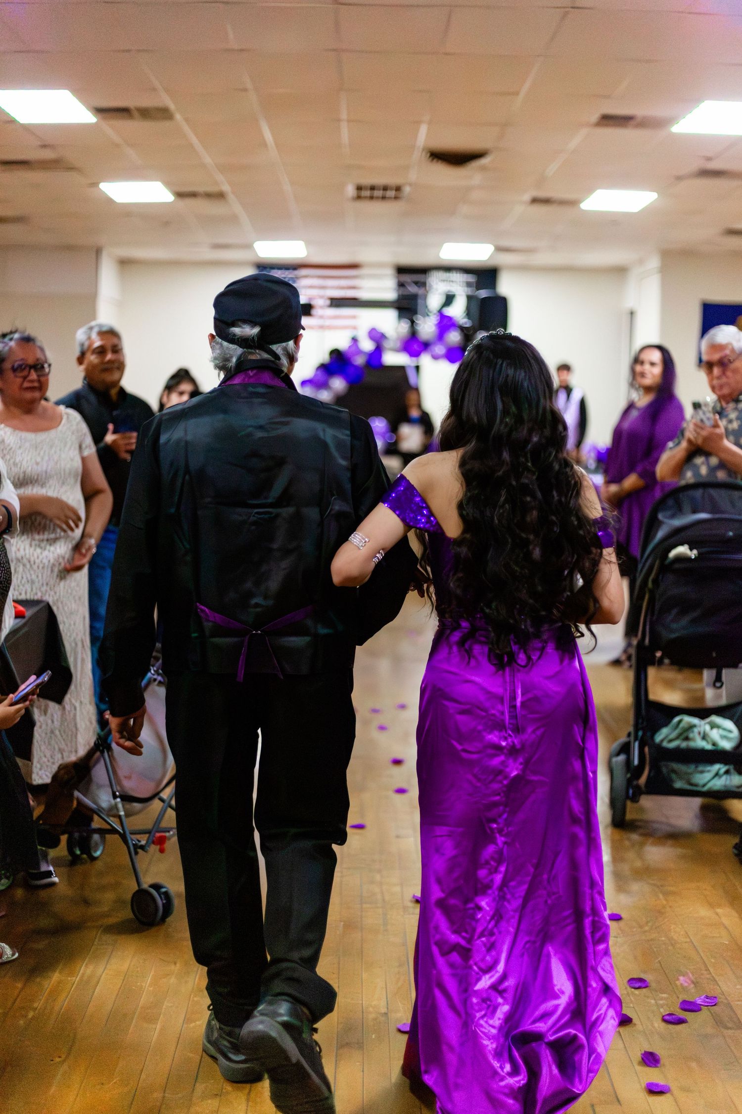Couple in formal attire walking down aisle, woman in purple gown, man in black suit, at an elegant event.