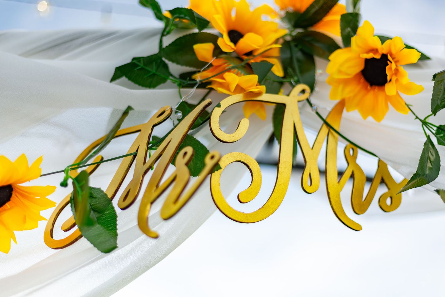 Gold Mr & Mrs sign with sunflower garland decor on white table at wedding reception.