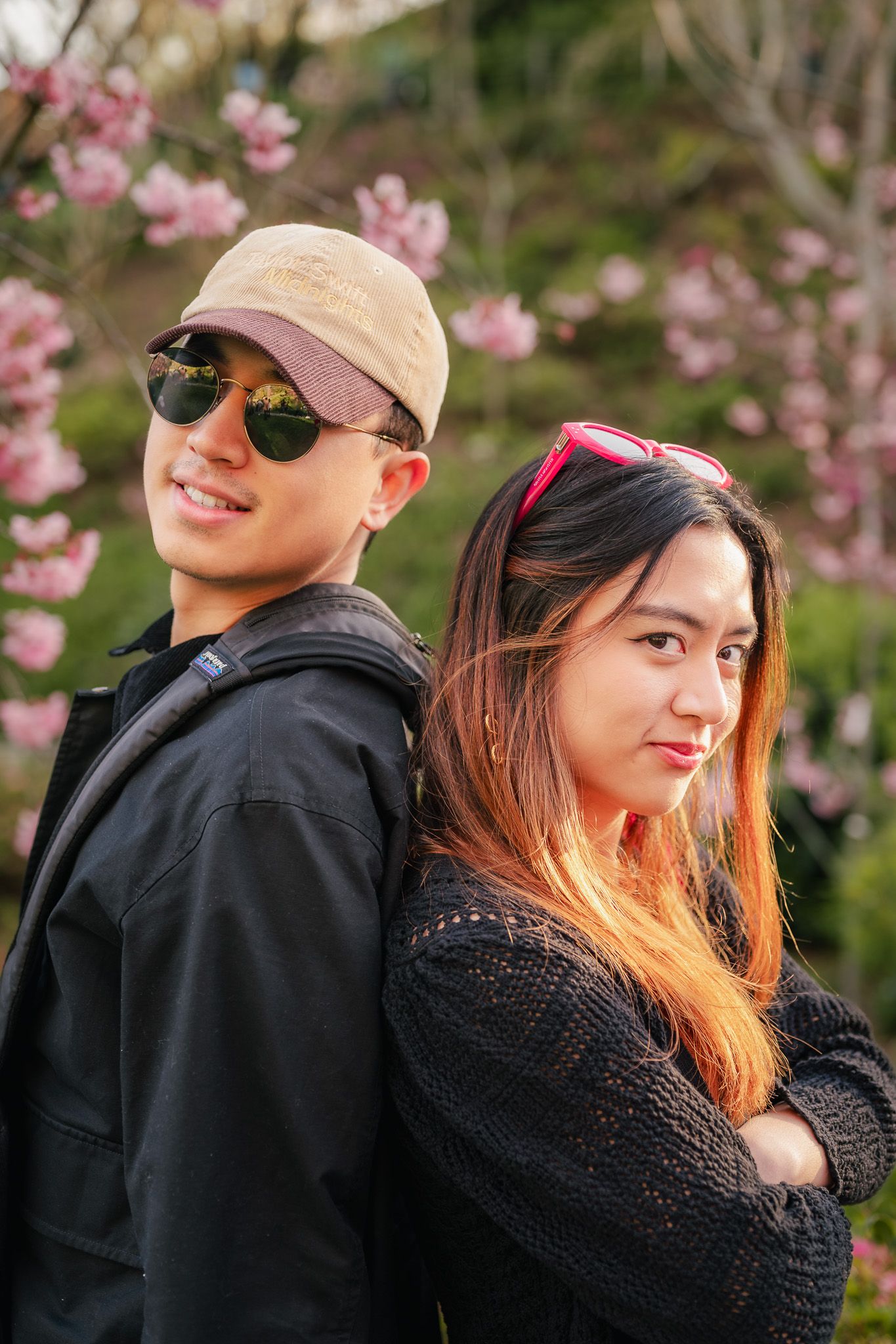 Portrait of a brother and sister duo leaning back-to-back in front of cherry blossoms at Balboa Park's Japanese Friendship Garden.