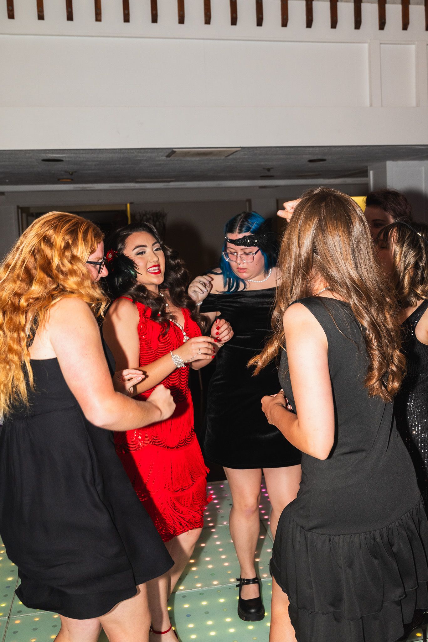 Full-body portrait of a woman in a red dress and her friends in black dresses on the dance floor at a 1920s themed party.