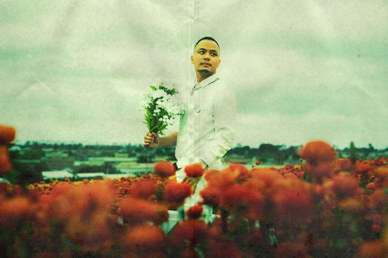 Full body portrait of Brandon wearing all white standing in a field of orange ranunculi at The Flower Fields at Carlsbad.
