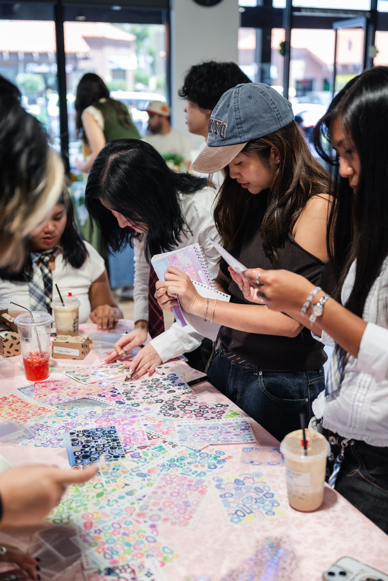 Portrait of a woman and her friends decorating their phone cases around a table sprawled with various sticker sheets.