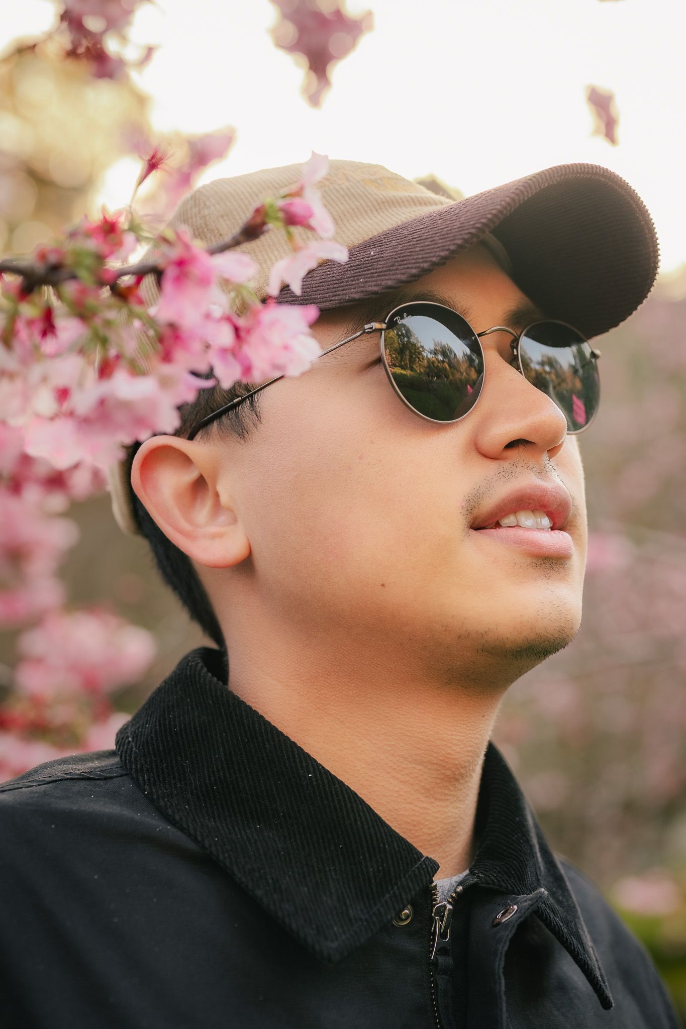 Up-close headshot of a man surrounded by cherry blossoms as he looks up and away to the right of the camera.