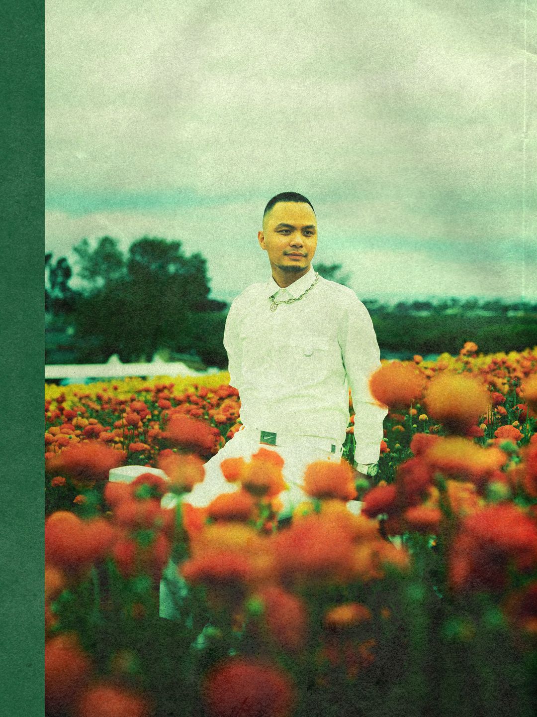 Portrait of Brandon wearing all white sitting in the middle of a field of orange ranunculi at The Flower Fields at Carlsbad.