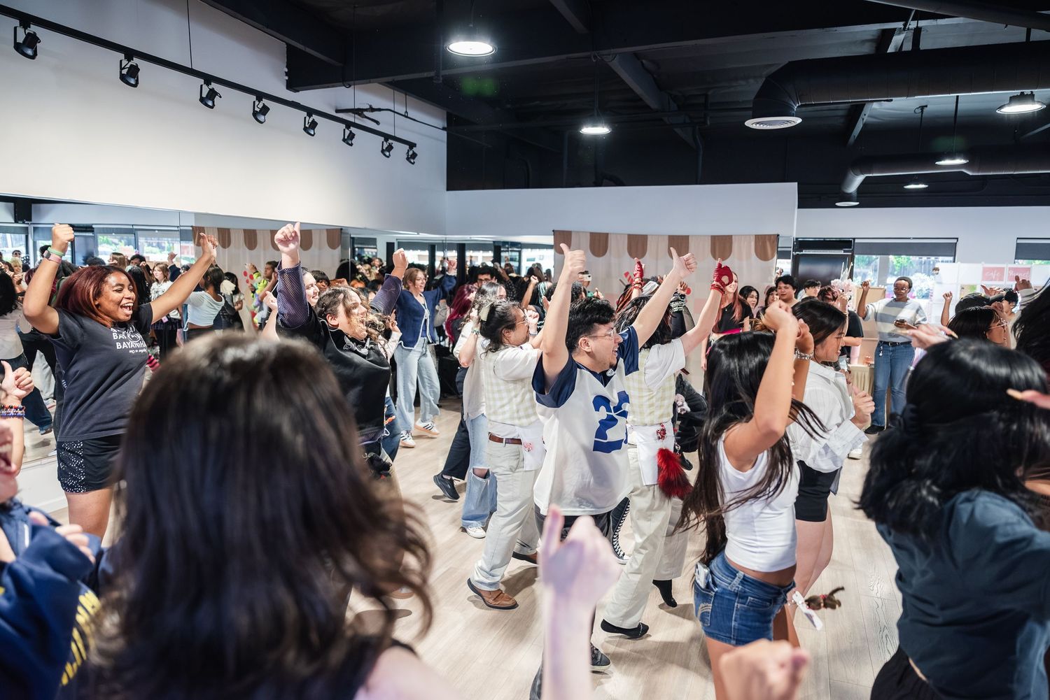 Portrait of a large group of people performing the same KPOP dance as others in the crowd cheer them on and wait for their turn.