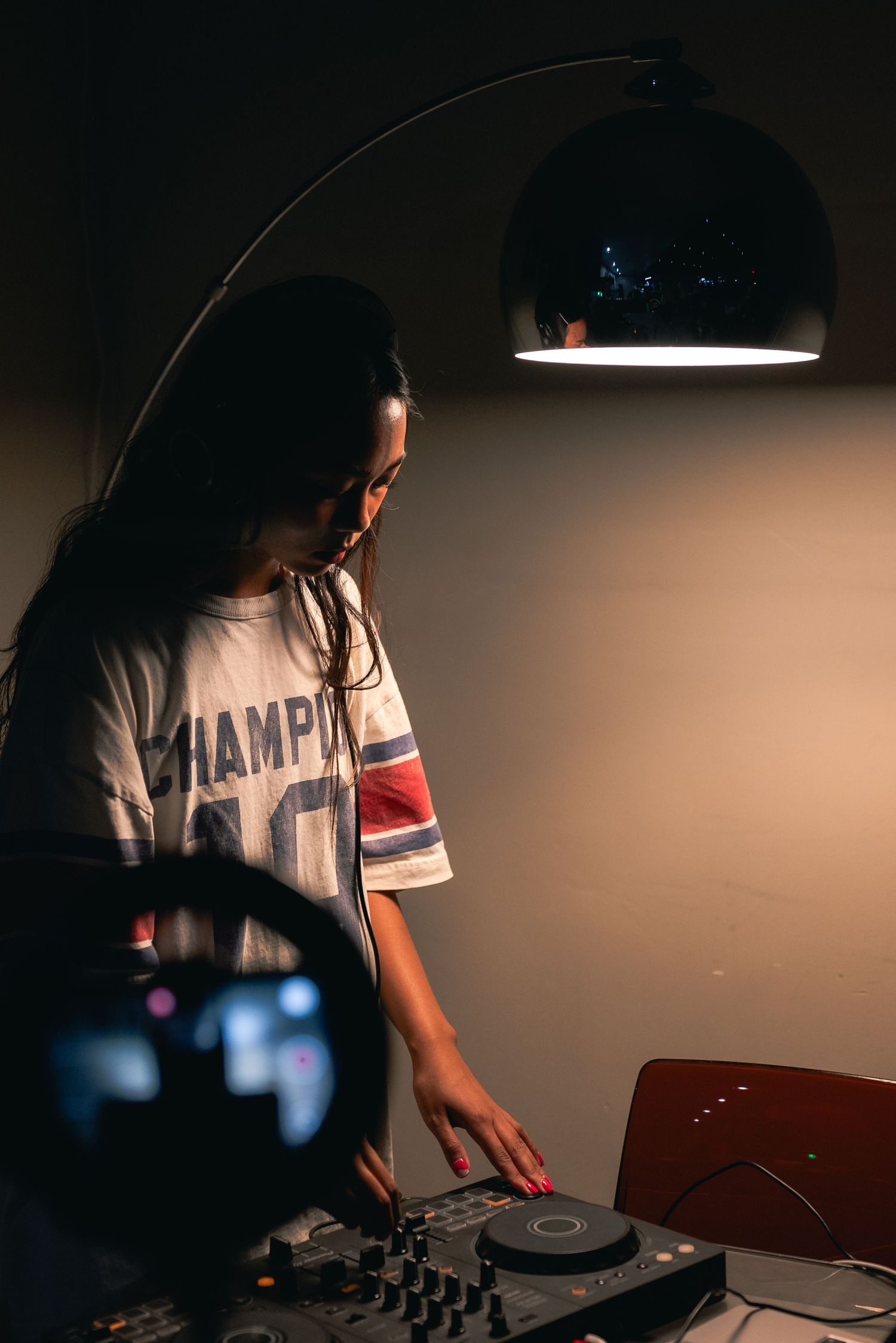 Portrait of a DJ dimly lit under a lamp as she prepares for her set.