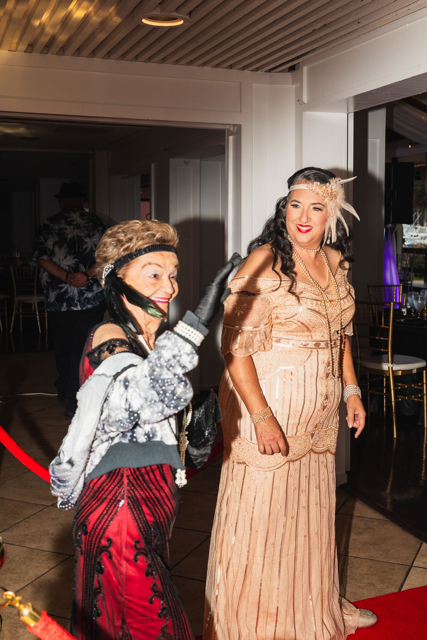 Full-body portrait of a mother and her grandmother dressed in 1920s apparel making their grand entrance to the party.