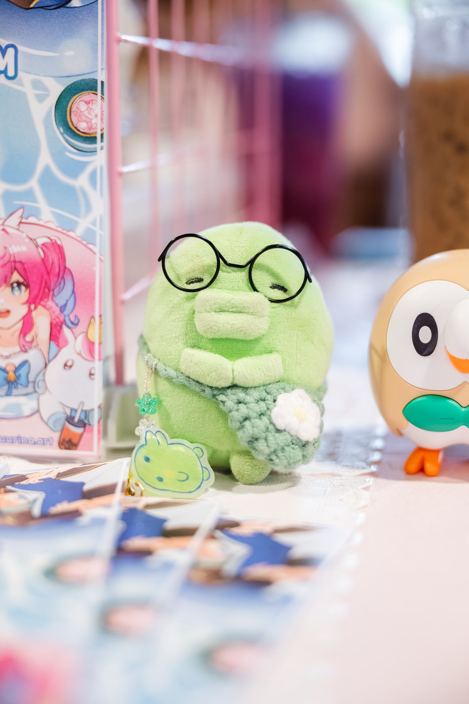 Detail shot of a smiling Kuchipachi plushie sitting on a vendor's table, surrounded by other trinkets and event praphernalia.