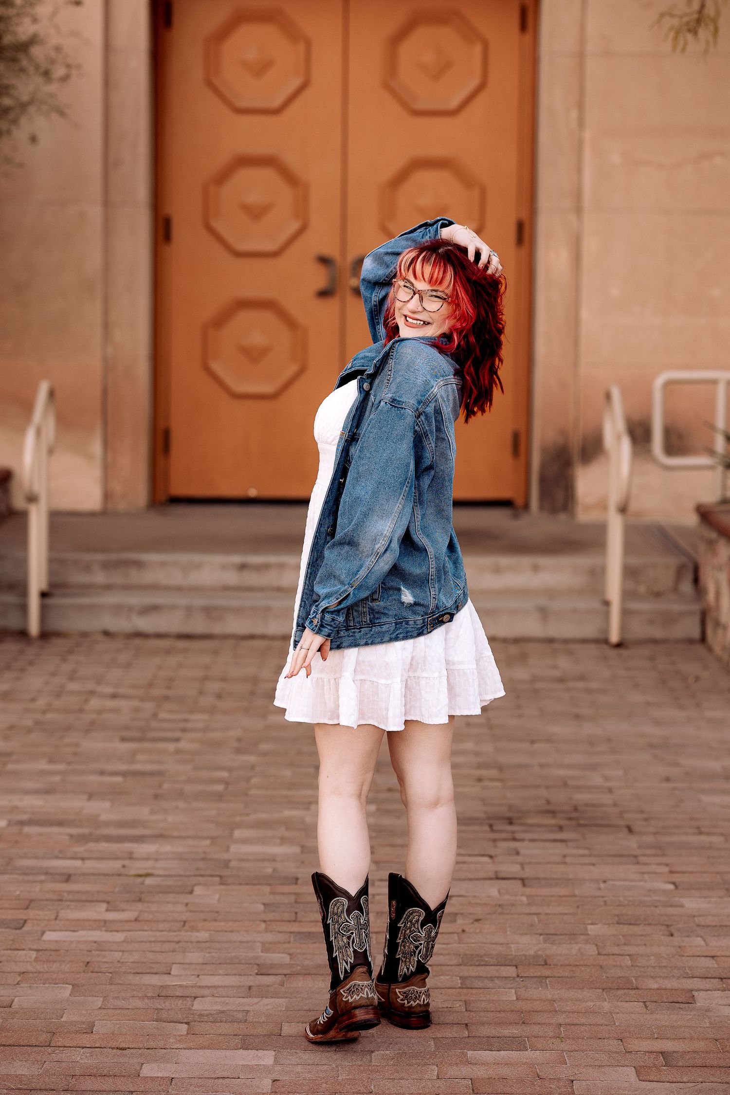 cute female senior during her senior pictures wearing a dress and boots with a jean jacket.