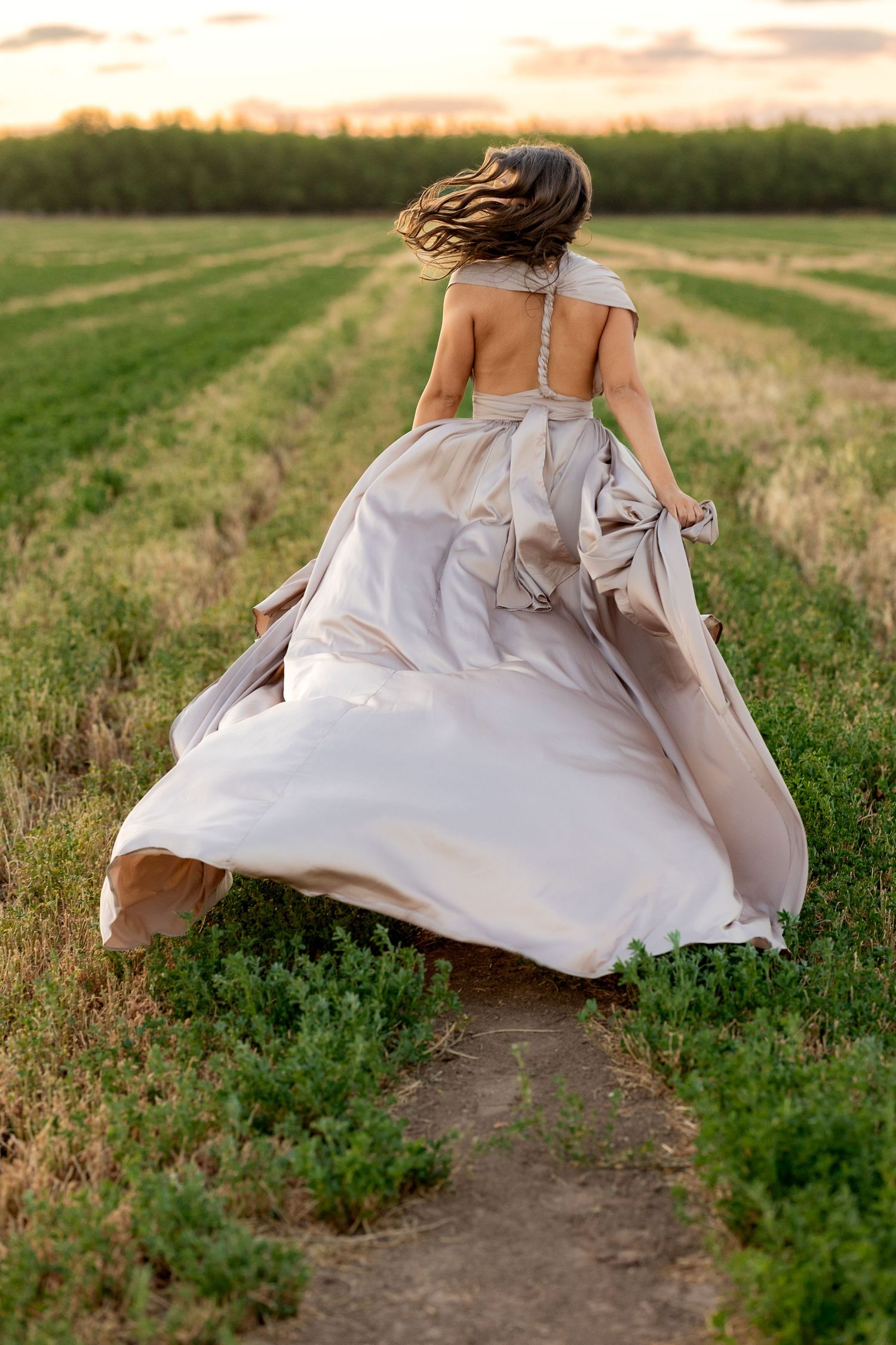 Female senior running through fa Missouri field in long romantic dress at sunset.