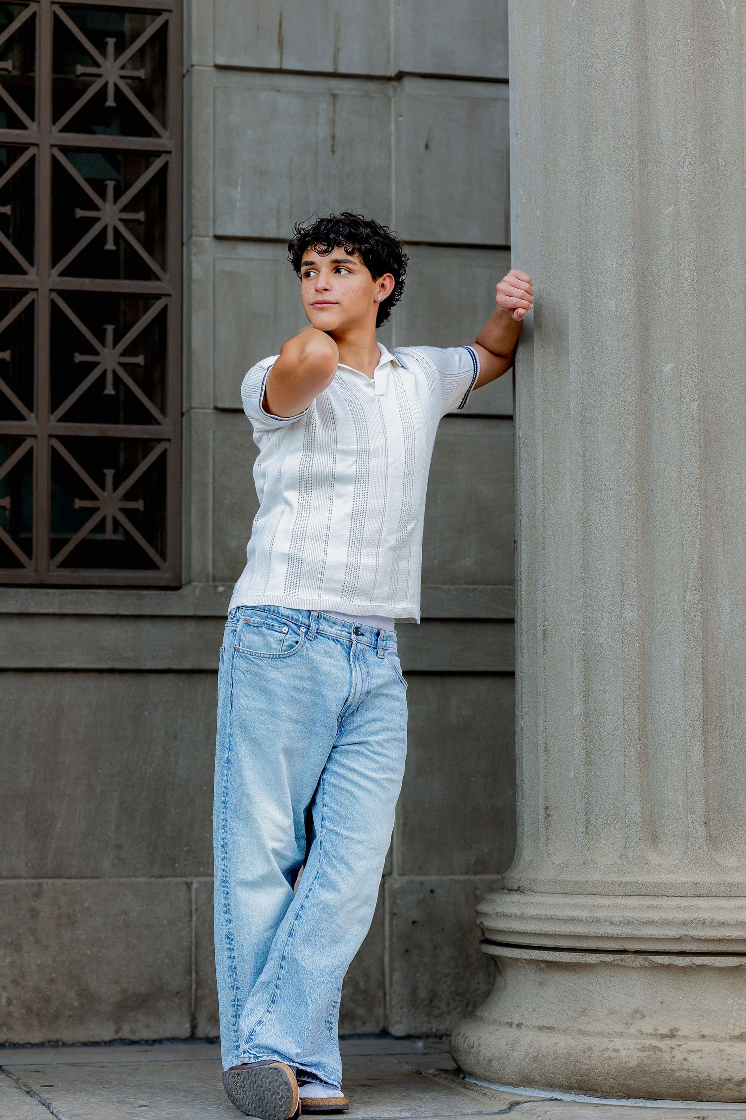 male senior during graduation pictures leaning against a column in the downtown area.