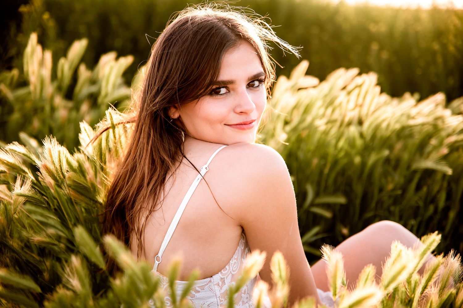 image of female high school senior during her Senior Portrait session sitting in tall grass in Southwest Missouri.