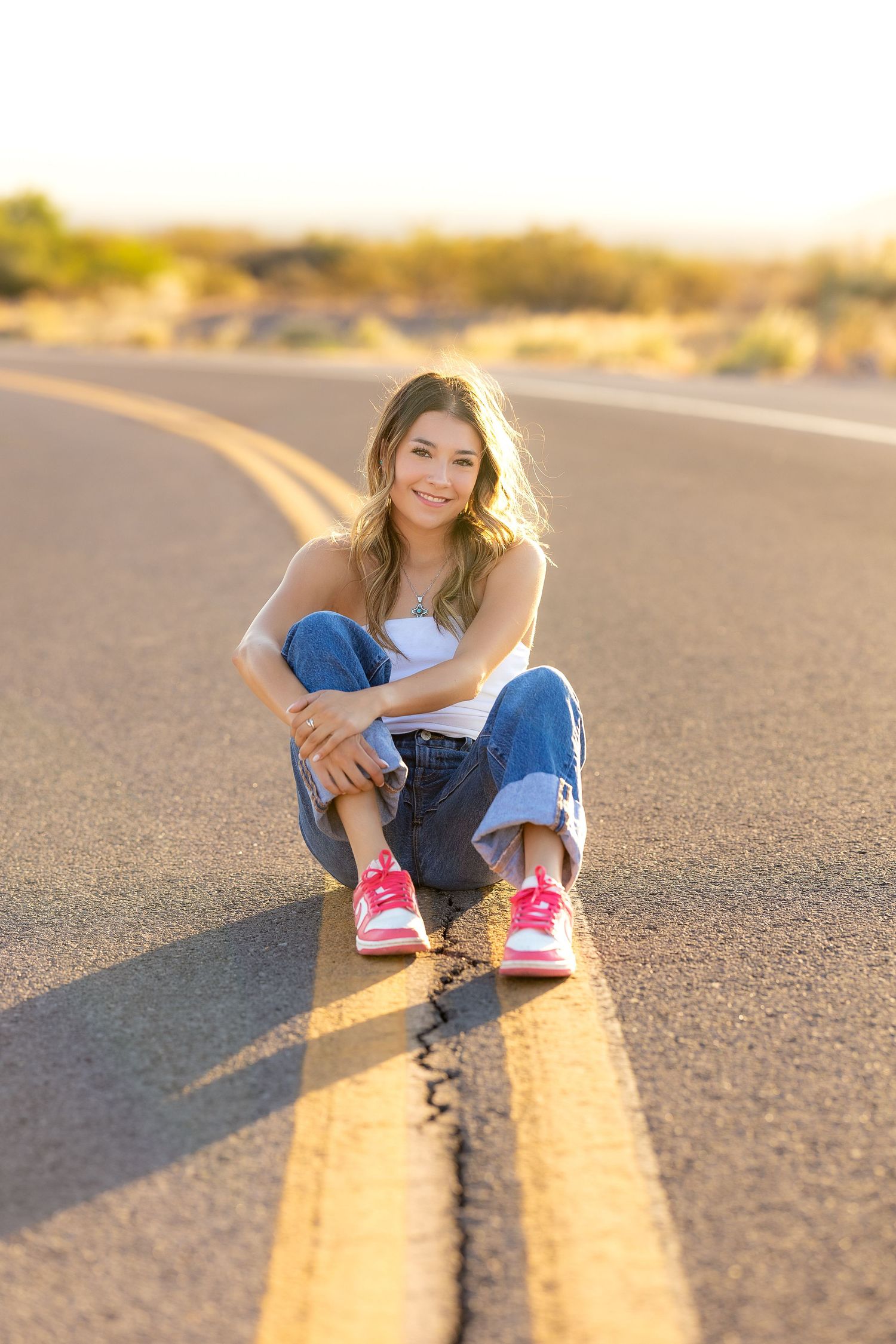 High School Senior during her Senior Portraits sitting on the yellow stripping in the middle of the road.
