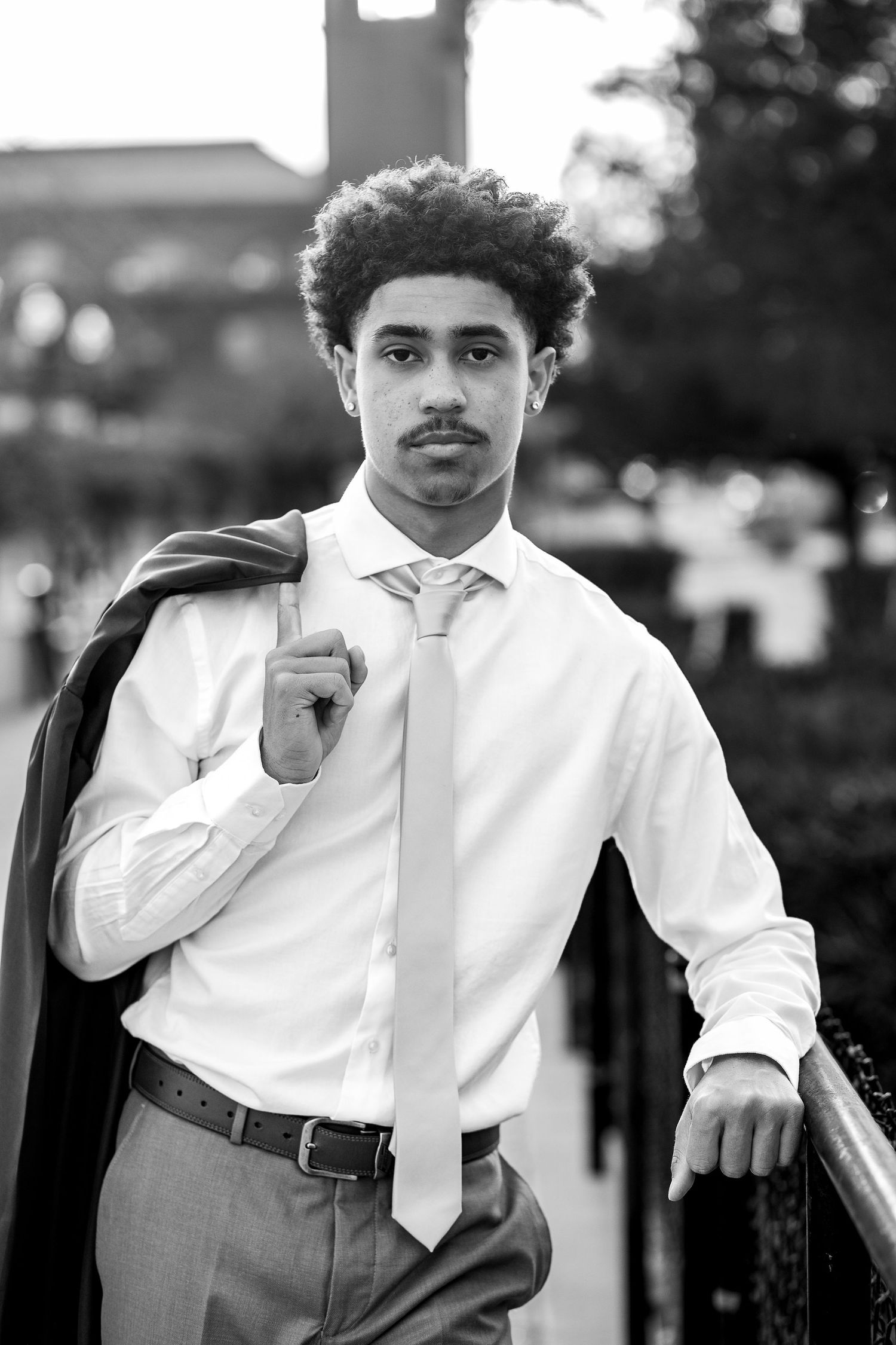 African American male High School Senior during his senior portraits, wearing a dress shirt and tie with a train station behind him.