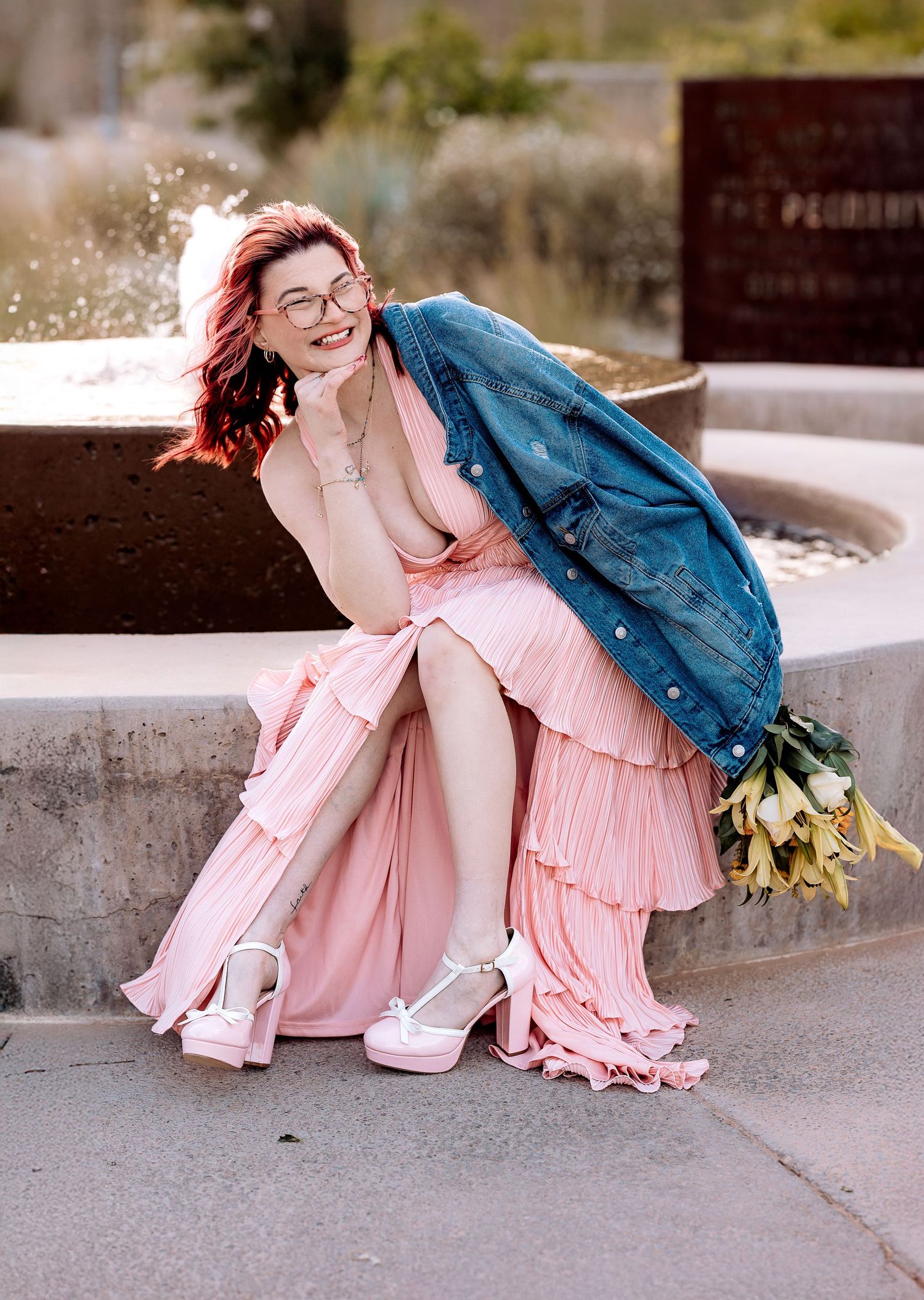Female Senior during her graduation pictures wearing a long pink gown while sitting in front of a fountain.