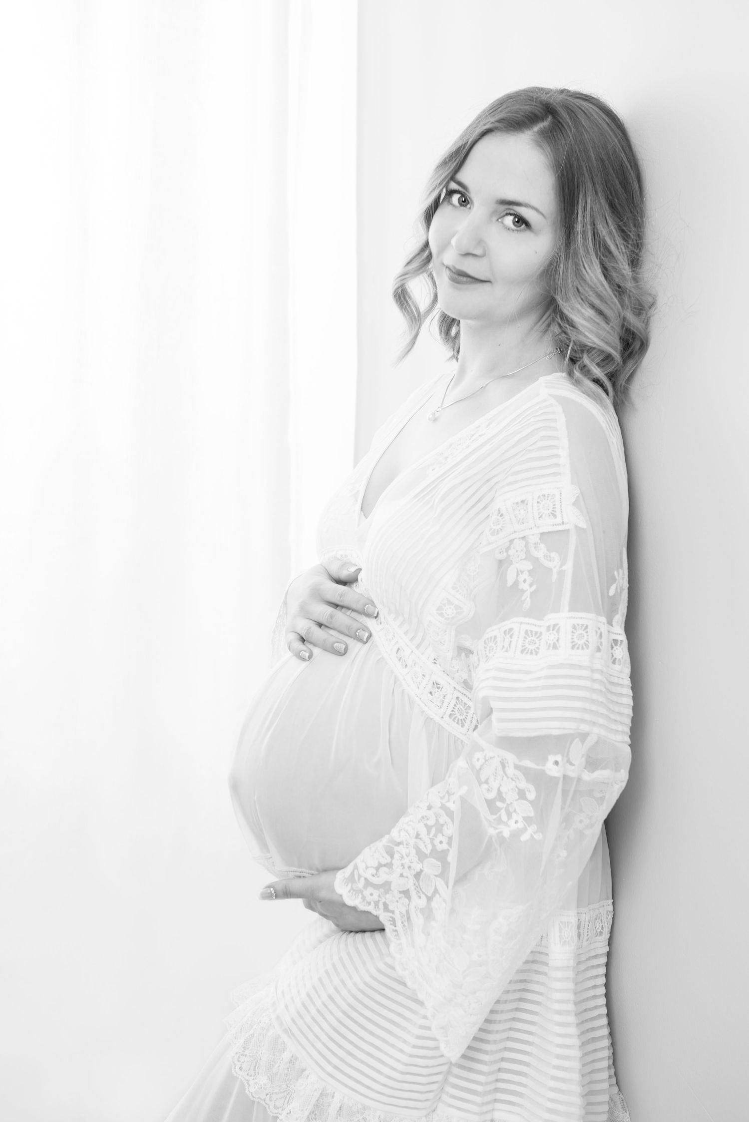 Maternity portraits featuring white lace dress against neutral background.