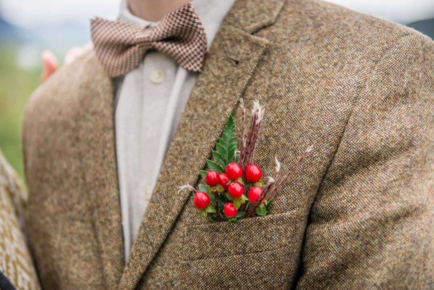 Close-up details of a brown tweed suit jacket with red berries and baby's breath boutonniere.