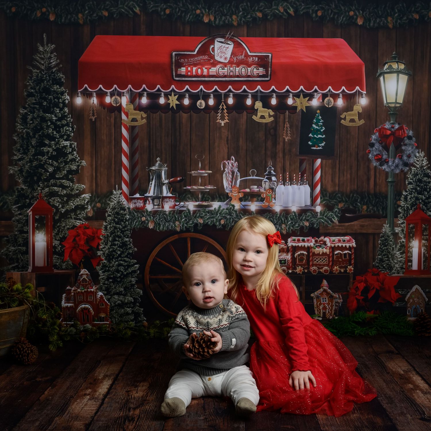 A festive Christmas photo setup with red decor, wooden floors, and holiday decorations against a dark backdrop.