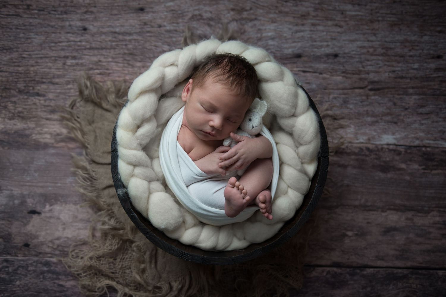 Peaceful newborn sleeping in cozy white nest with rustic wood background.