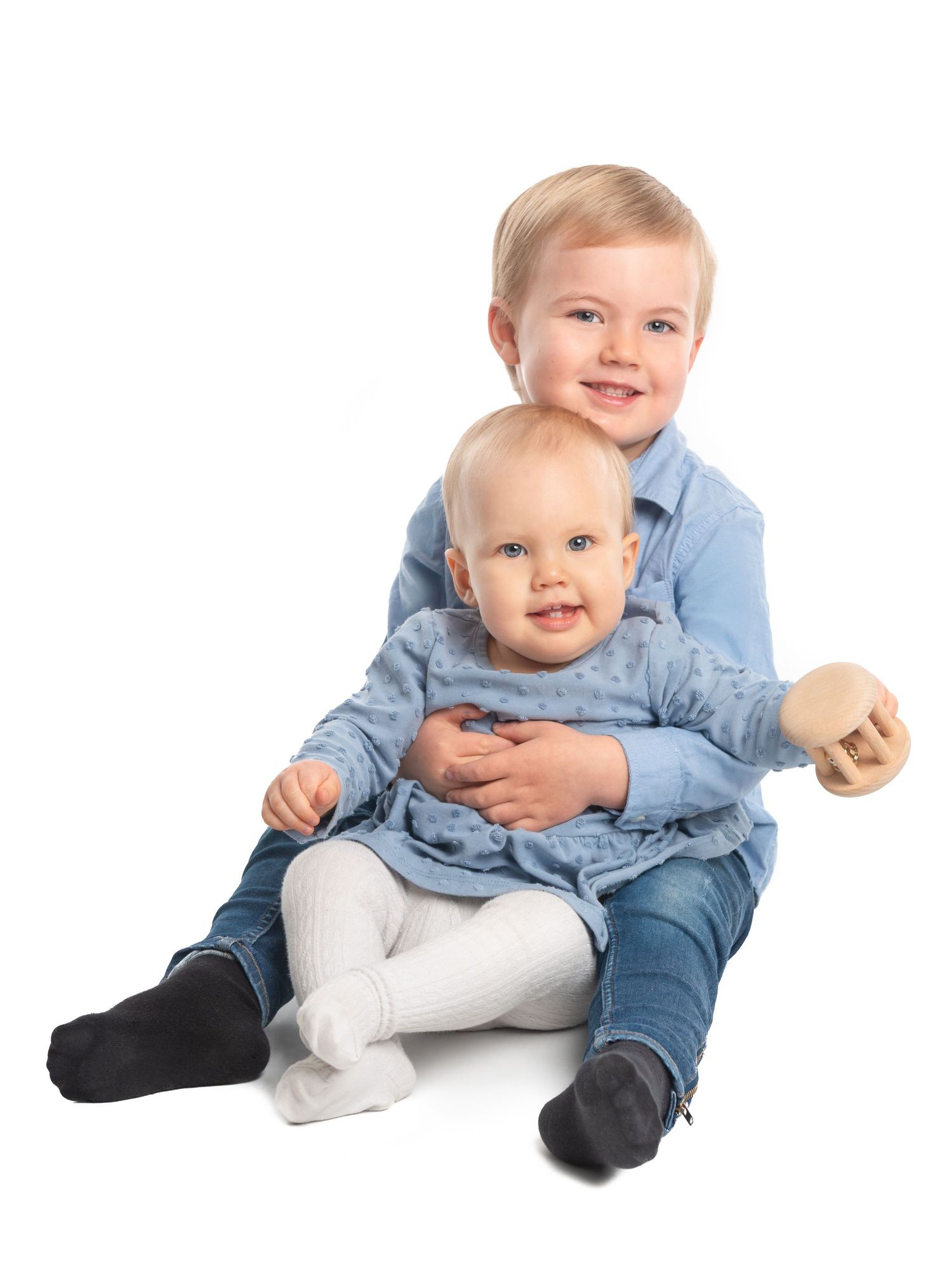 Baby wearing blue outfit sitting and smiling on white studio background.