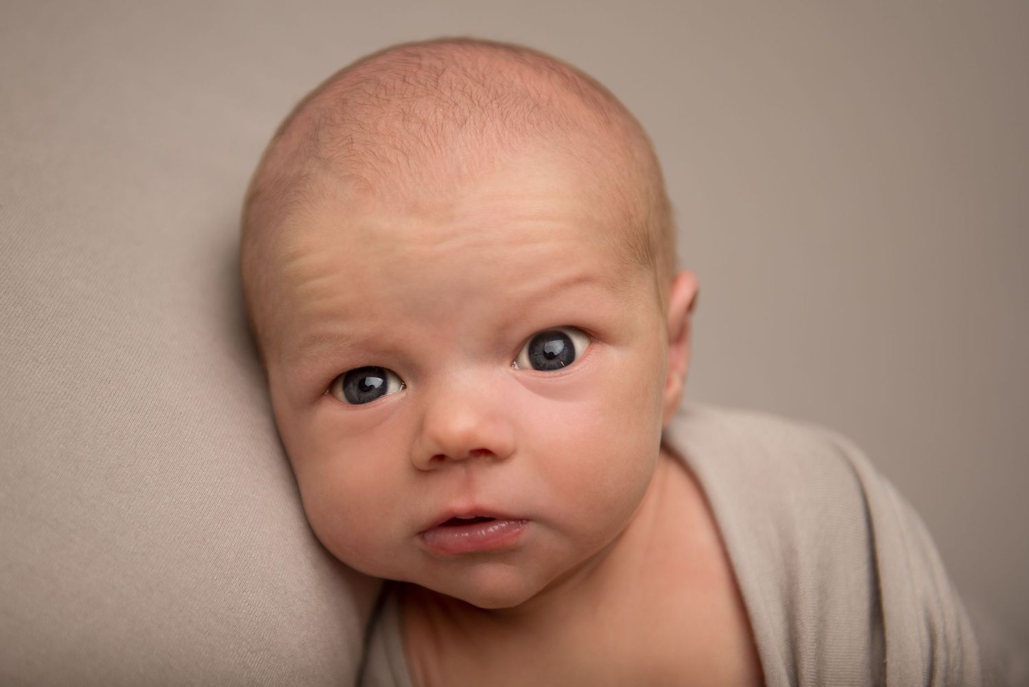 Sleeping newborn wrapped in beige fabric against neutral backdrop in professional portrait.