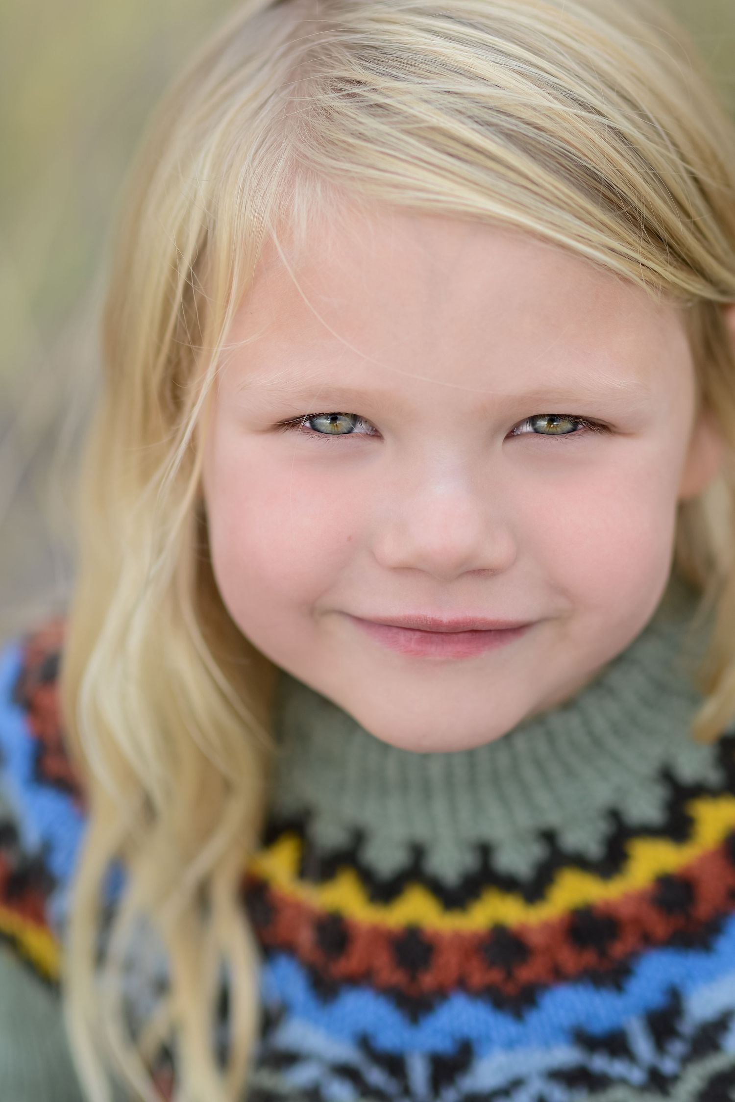 Close-up portrait of a blonde girl with green eyes wearing a colorful Fair Isle turtleneck sweater.