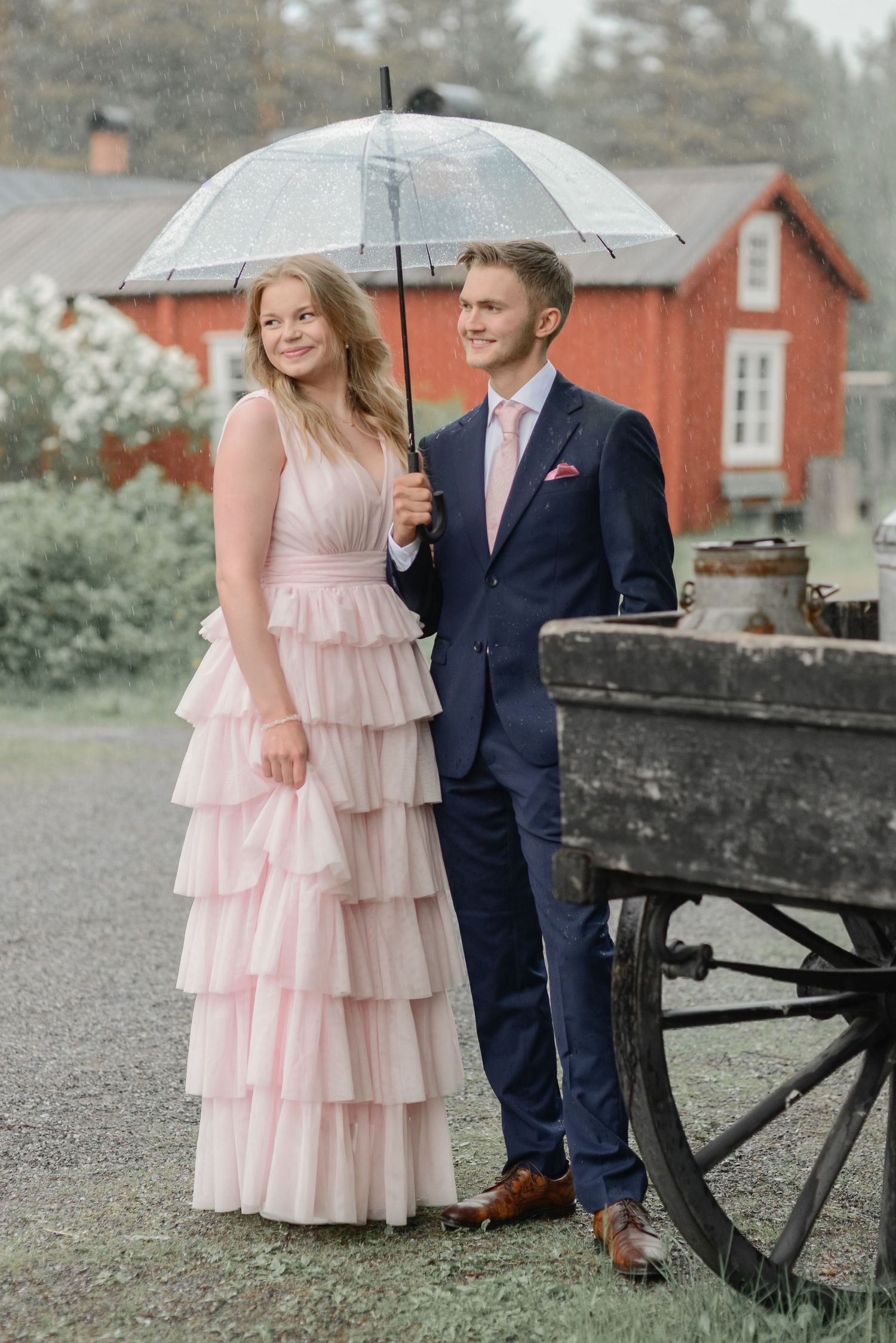 A romantic photoshoot featuring a pink tiered dress and navy suit near an antique wagon.