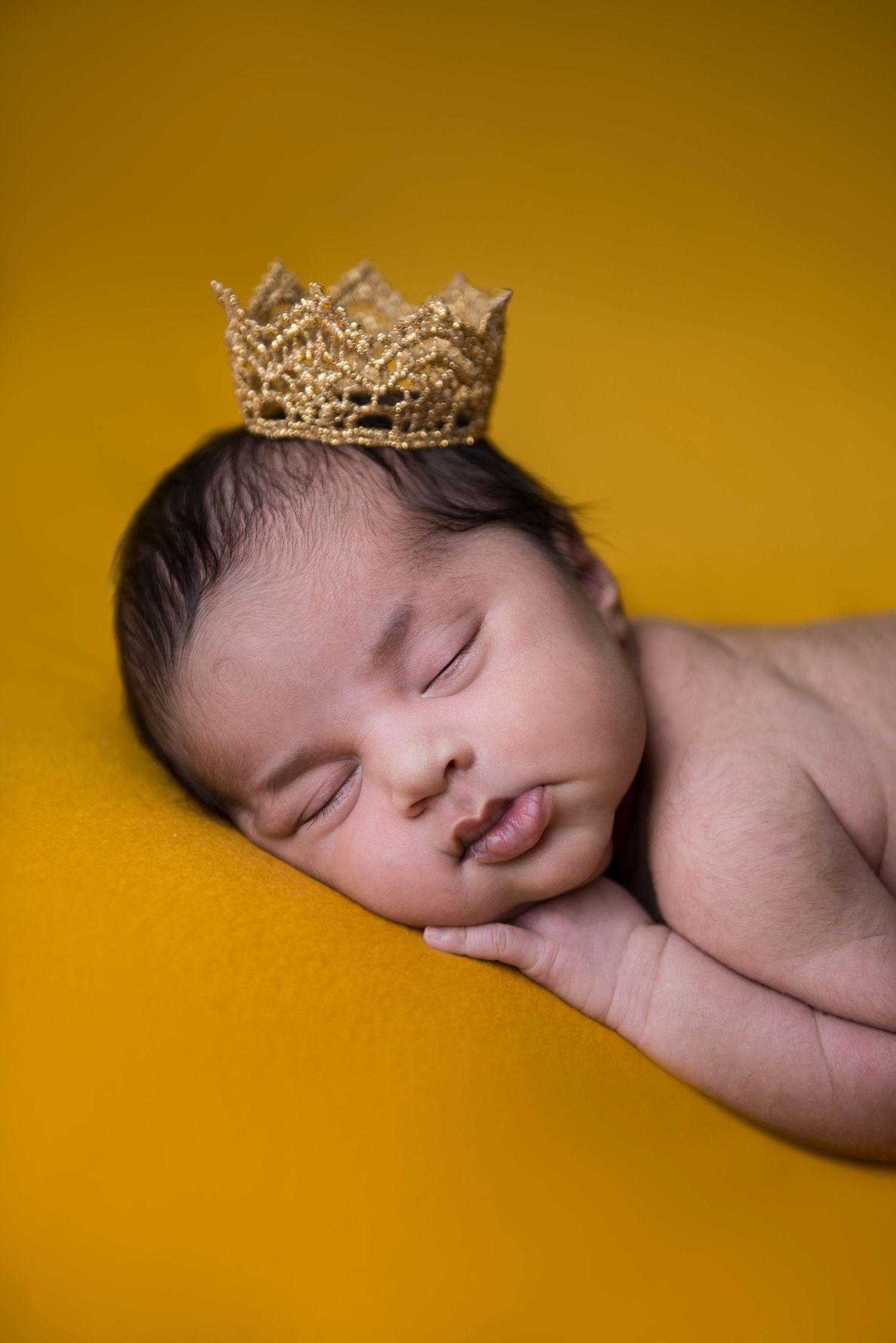 Sleeping newborn wearing delicate crown on yellow background in artistic portrait.
