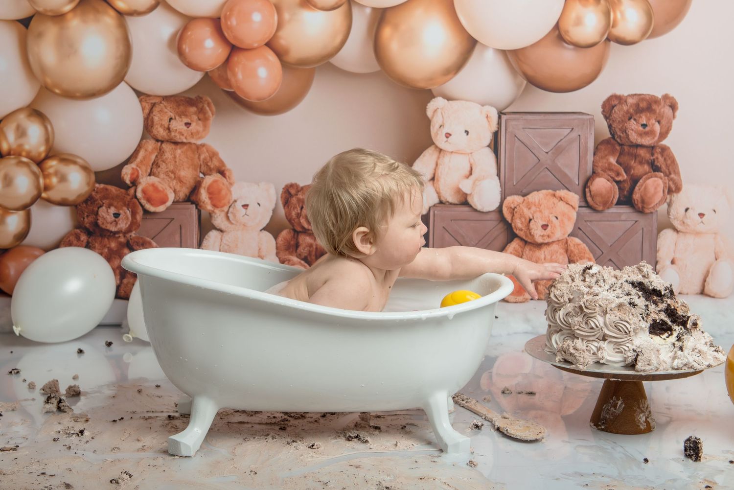 A baby sits in a white bathtub during a cake smash photo session cleanup.