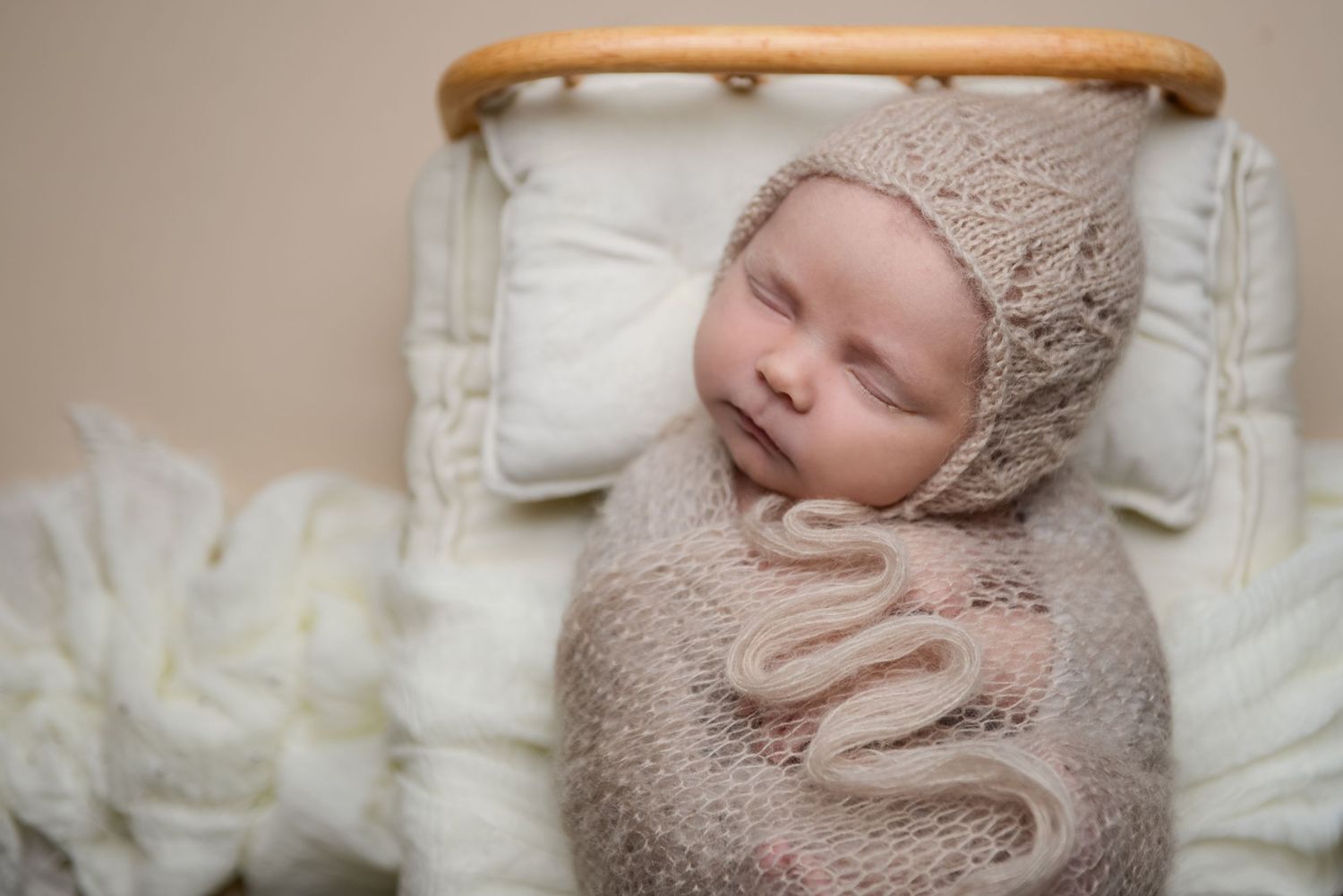 Newborn wrapped in soft beige knit blanket sleeping in wooden prop basket.