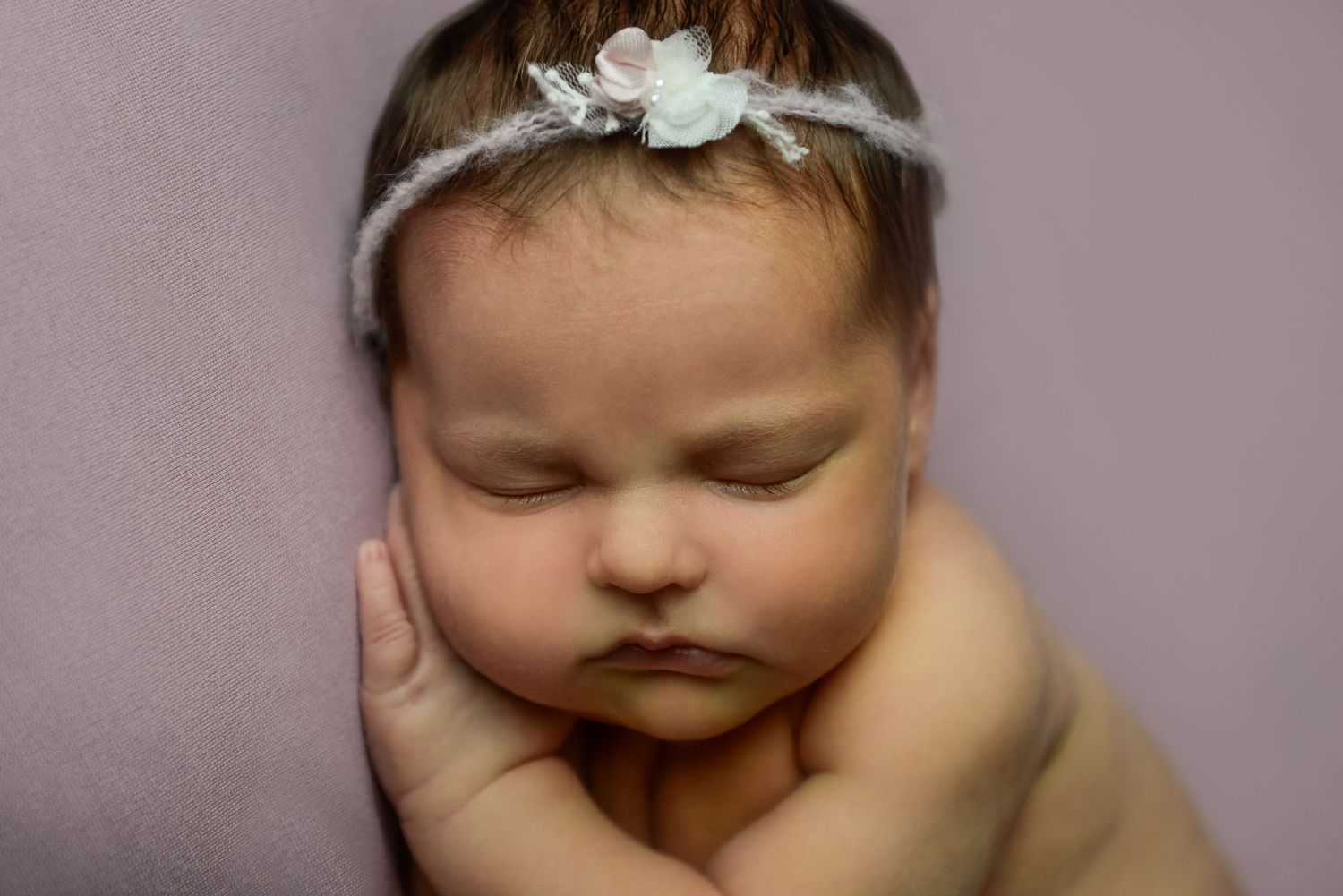 Dreamy portrait of sleeping newborn with delicate headpiece in soft lighting.