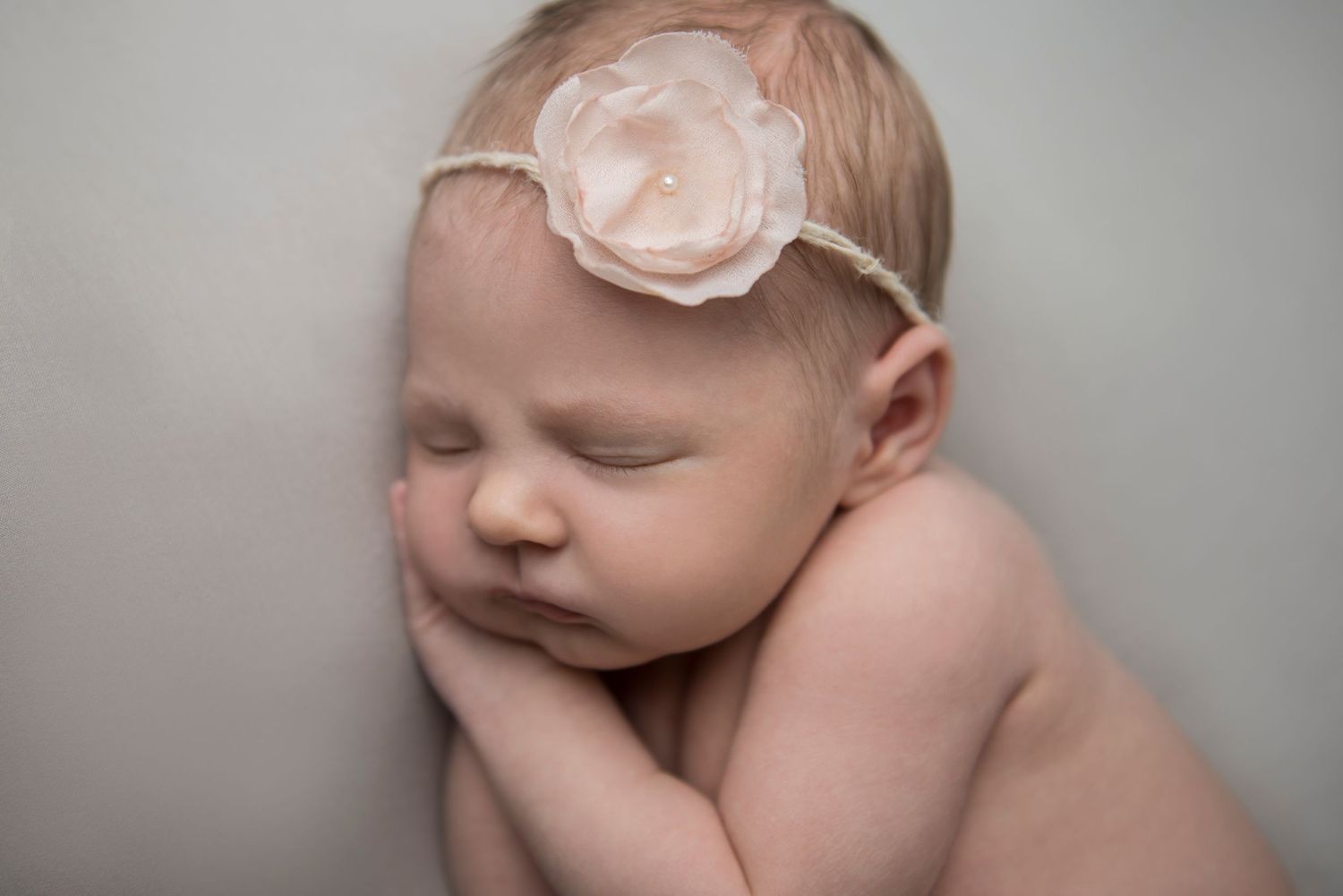 Artistic portrait of newborn with delicate floral accessory against neutral background.