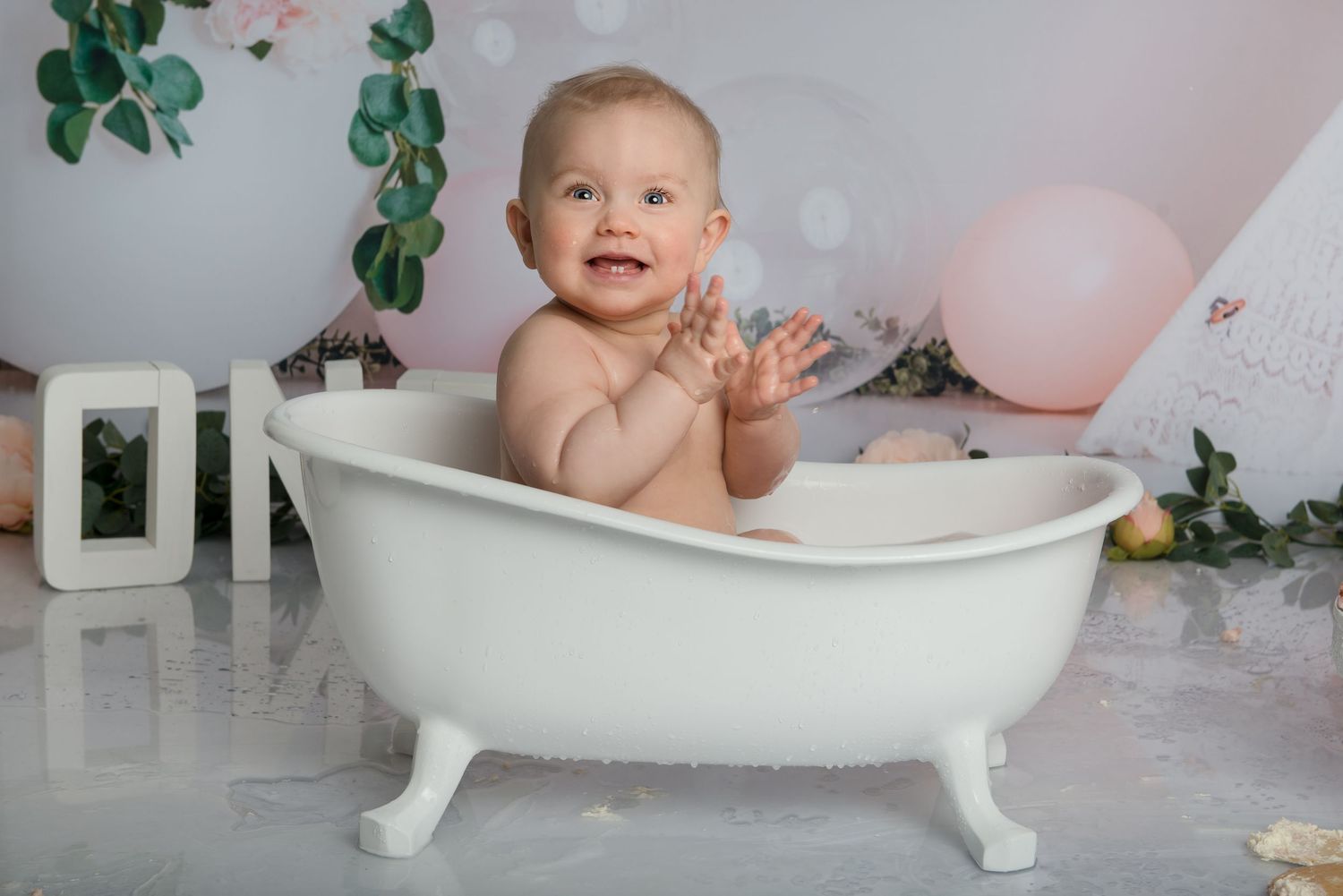 First birthday photoshoot setup with white clawfoot tub, balloons and greenery decorations.