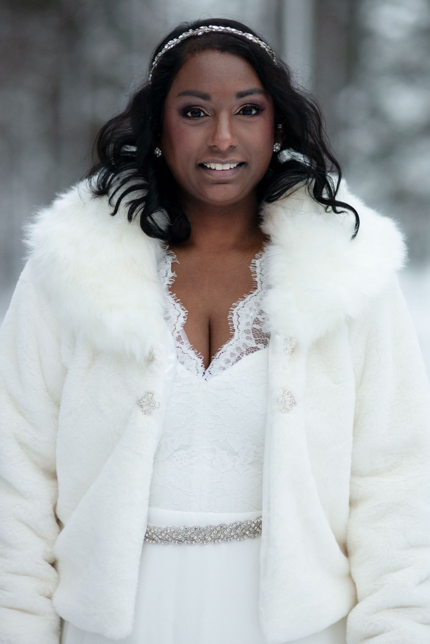 Winter bride wearing an elegant white fur coat and lace dress in snowy setting.
