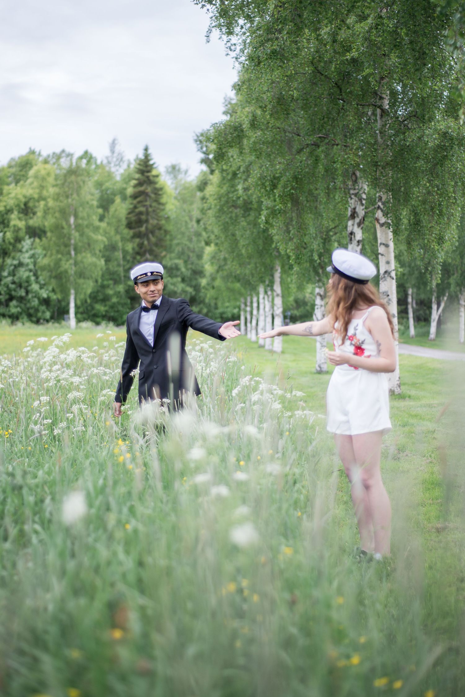 Couple walking through a meadow with white flowers and birch trees on a summer day.