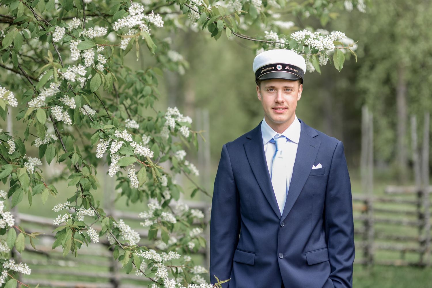 Formal portrait under flowering tree branches in navy suit.