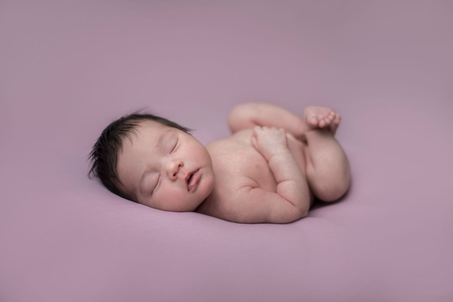 Artistic newborn portraits on soft purple backdrop showing peaceful sleeping poses.