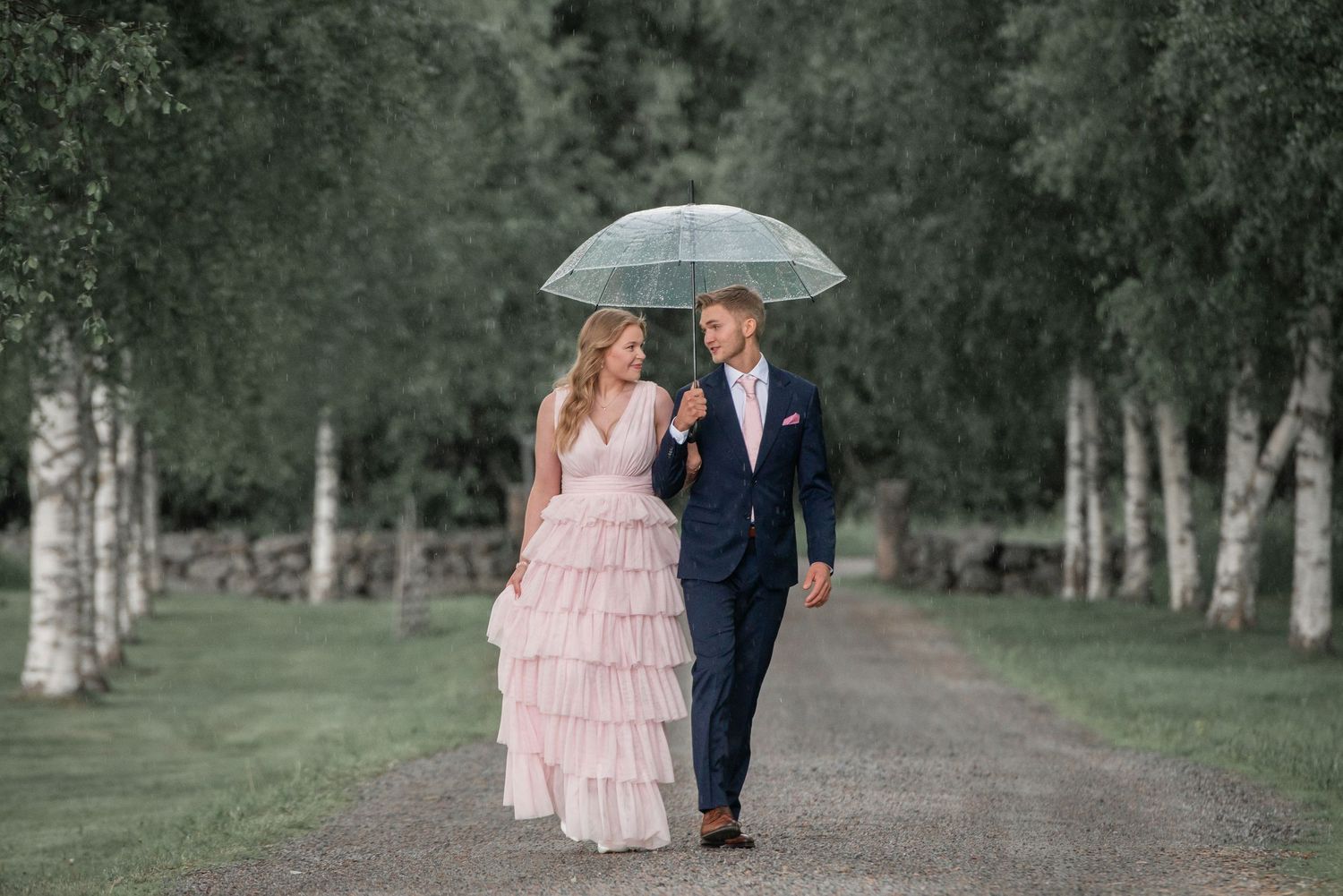 A couple shares intimate moments under an umbrella along a tree-lined path.
