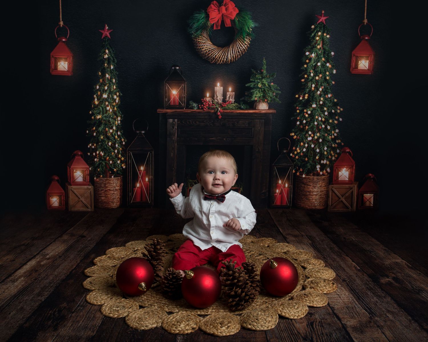 Holiday photo scene with red ornaments, miniature trees and vintage lanterns on wooden flooring.