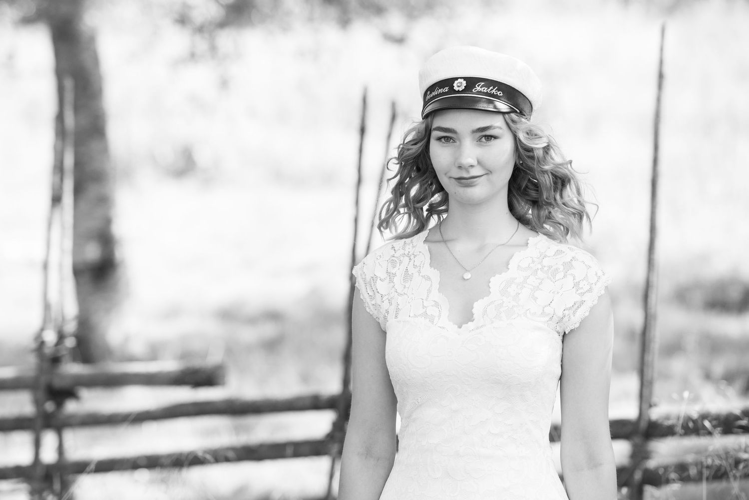 Black and white portrait series in a lace white dress and sailor cap against a natural outdoor background.